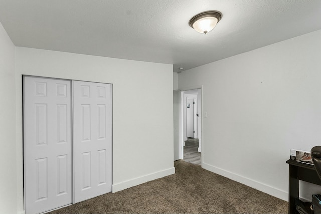 unfurnished bedroom with dark colored carpet, a closet, a textured ceiling, and baseboards