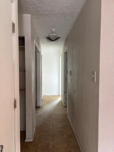 hallway with a textured ceiling and dark tile patterned floors