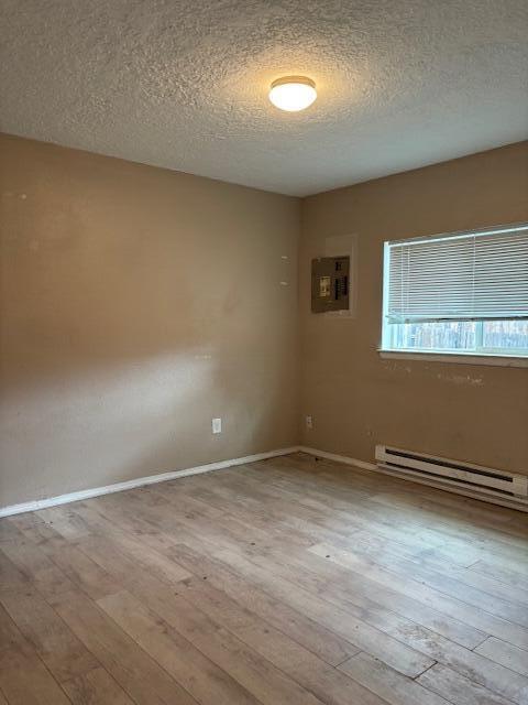 empty room featuring a textured ceiling, a baseboard radiator, baseboards, electric panel, and hardwood / wood-style floors