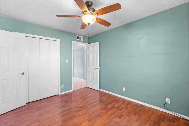 unfurnished bedroom with baseboards, visible vents, wood finished floors, a textured ceiling, and a closet