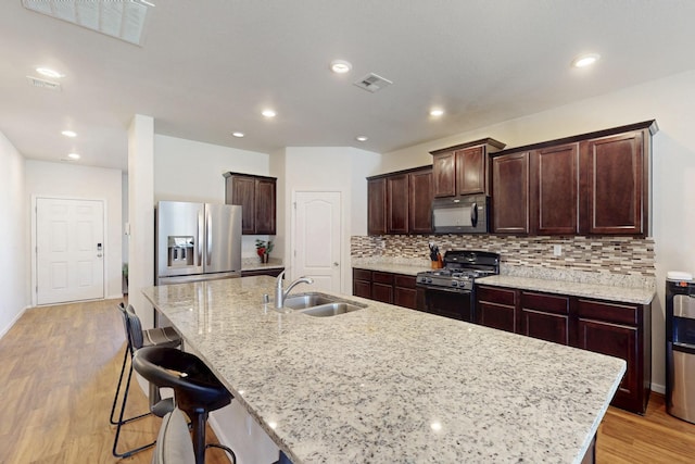 kitchen with visible vents, decorative backsplash, light wood-style flooring, black appliances, and a sink