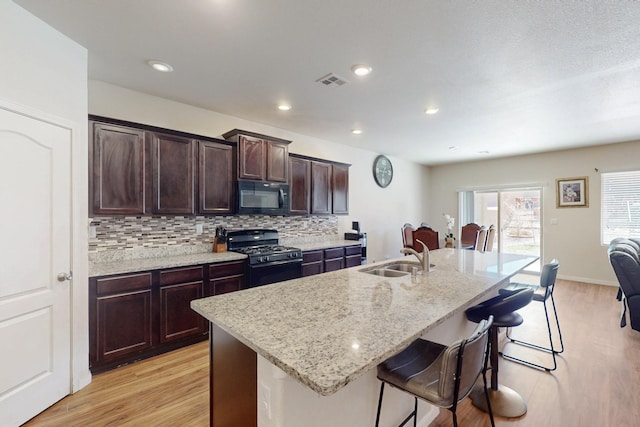 kitchen featuring a sink, visible vents, a kitchen breakfast bar, decorative backsplash, and black appliances