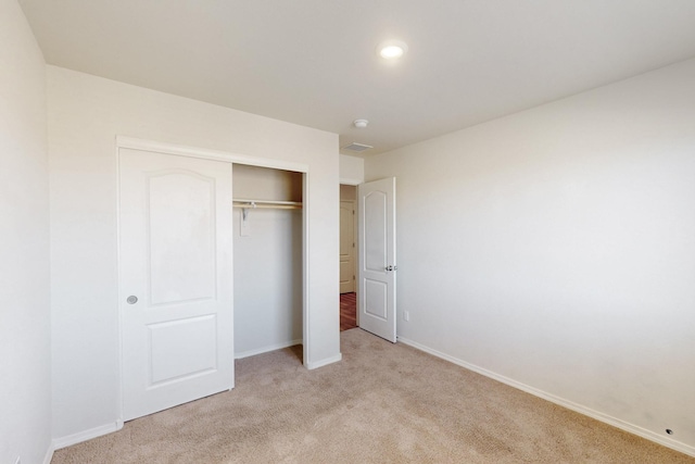 unfurnished bedroom featuring light carpet, a closet, visible vents, and baseboards