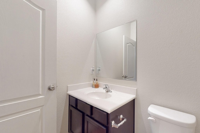 bathroom with a textured wall, vanity, and toilet