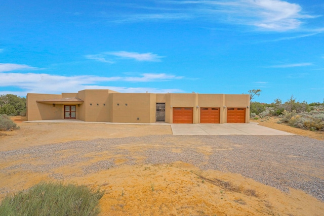 pueblo-style home with stucco siding, gravel driveway, and a garage