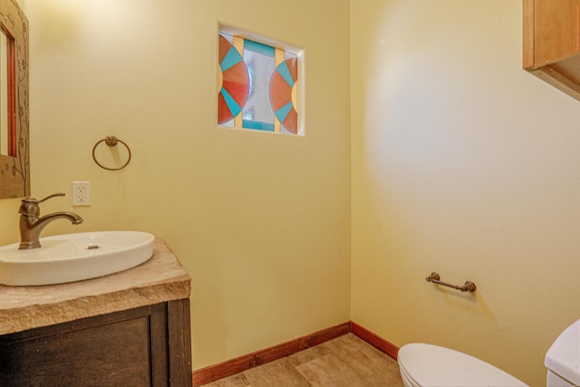 half bathroom with toilet, vanity, and baseboards