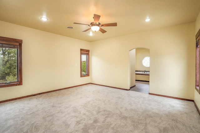 empty room featuring carpet flooring, baseboards, arched walkways, and ceiling fan