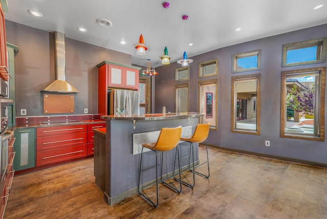 kitchen featuring visible vents, stainless steel refrigerator with ice dispenser, stainless steel counters, wall chimney range hood, and dark brown cabinets