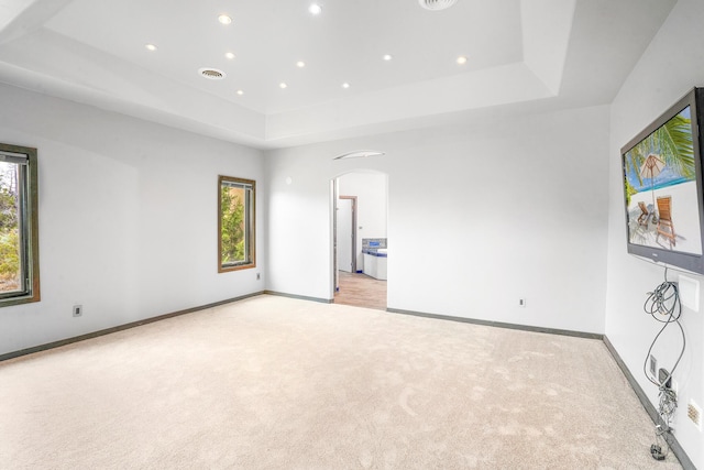 unfurnished bedroom with baseboards, a tray ceiling, recessed lighting, arched walkways, and light carpet