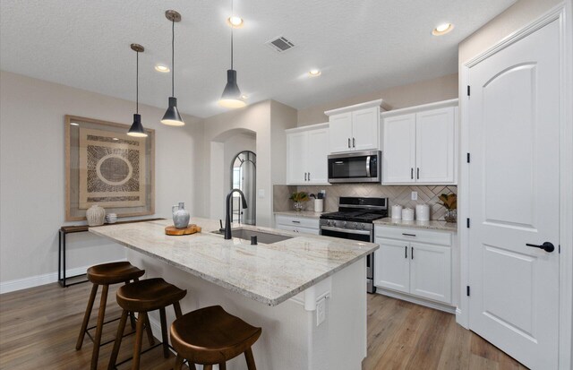 938 Lazuli Rd SE, Rio Rancho, NM 87124 - kitchen featuring tasteful backsplash, visible vents, an island with sink, arched walkways, and stainless steel appliances