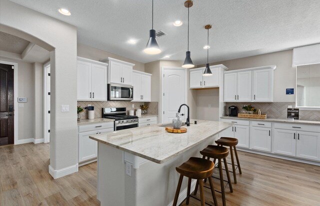 938 Lazuli Rd SE, Rio Rancho, NM 87124 - kitchen featuring a center island with sink, appliances with stainless steel finishes, arched walkways, white cabinetry, and a sink
