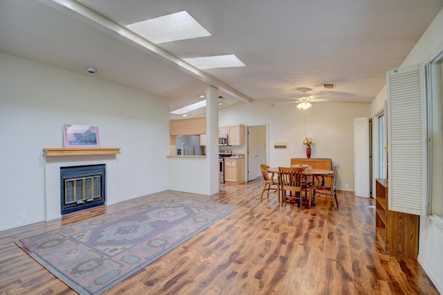 dining room with vaulted ceiling with skylight, a ceiling fan, baseboards, light wood finished floors, and a glass covered fireplace