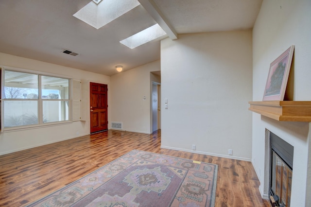 living area featuring baseboards, visible vents, a glass covered fireplace, lofted ceiling with skylight, and wood finished floors