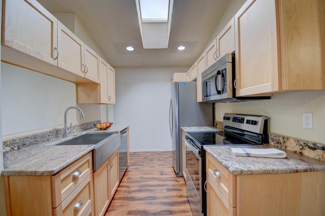 kitchen with stainless steel appliances, light brown cabinetry, a skylight, and light wood-style flooring