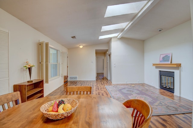 dining area featuring a glass covered fireplace, lofted ceiling with skylight, wood finished floors, and visible vents