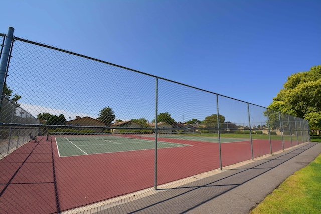 view of community featuring a tennis court, fence, and a yard