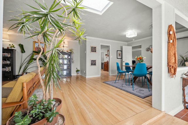 dining room featuring baseboards, a skylight, ornamental molding, and wood finished floors