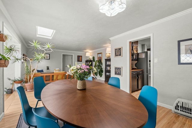 dining area featuring a skylight, baseboards, heating unit, ornamental molding, and light wood-style flooring