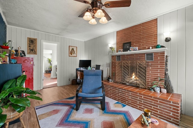 interior space with a ceiling fan, a brick fireplace, a textured ceiling, and wood finished floors