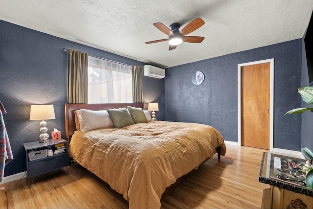 bedroom featuring light wood-type flooring, a wall mounted air conditioner, and a textured wall