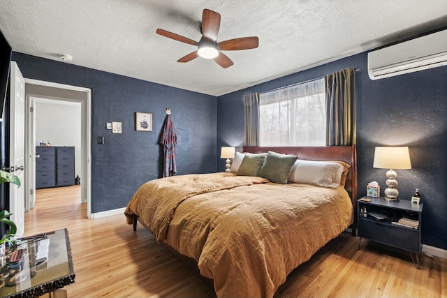 bedroom featuring a textured wall, light wood-style flooring, baseboards, and a wall mounted air conditioner