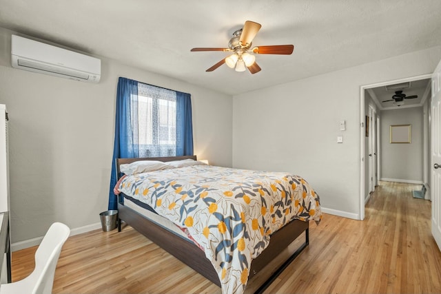 bedroom with baseboards, a wall mounted air conditioner, light wood-style flooring, and a ceiling fan