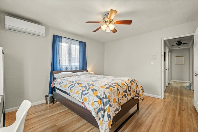 bedroom with a wall mounted air conditioner, light wood-style flooring, and baseboards