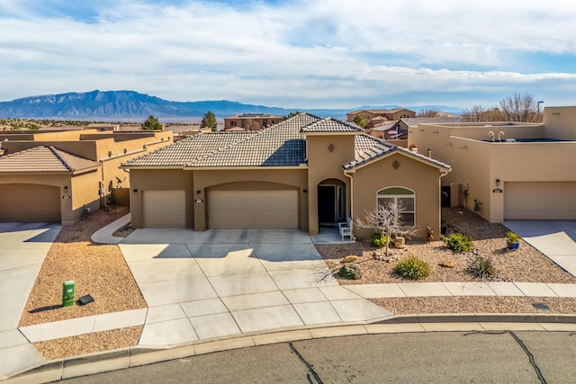 view of front facade featuring a tiled roof, concrete driveway, stucco siding, a garage, and a mountain view