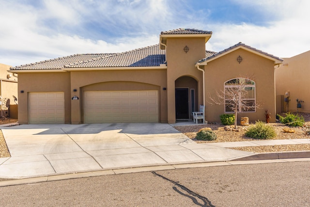 mediterranean / spanish house with concrete driveway, a tiled roof, an attached garage, and stucco siding