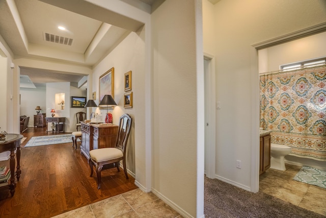 hallway with visible vents, a raised ceiling, and baseboards