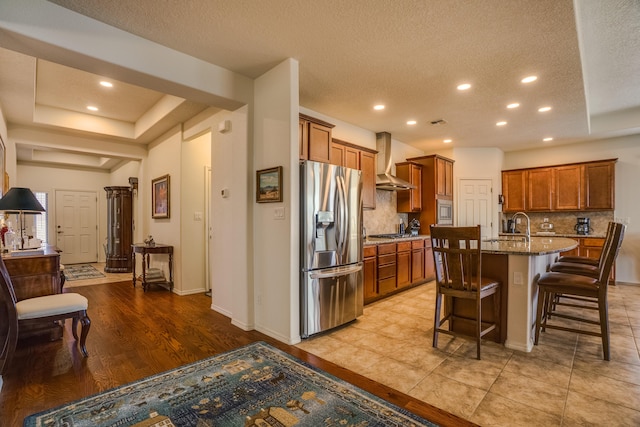 kitchen with dark stone counters, a breakfast bar area, brown cabinets, stainless steel appliances, and wall chimney exhaust hood