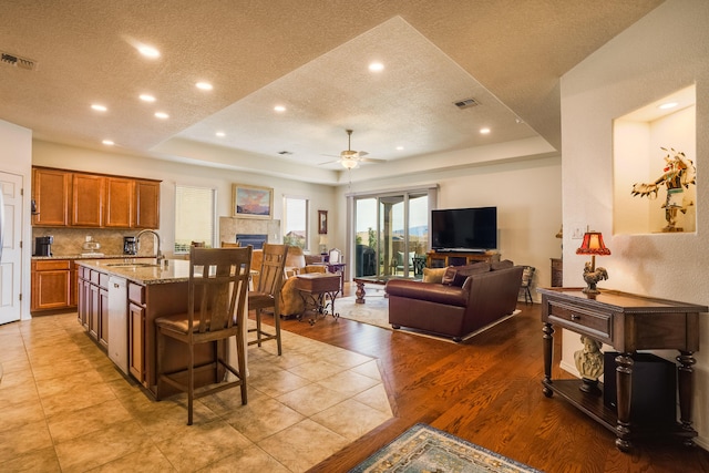 kitchen with a tray ceiling, light stone countertops, open floor plan, and brown cabinetry