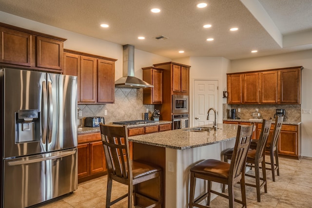 kitchen featuring a sink, stainless steel appliances, a kitchen bar, and wall chimney range hood