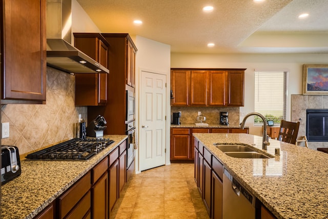 kitchen with a sink, light stone countertops, appliances with stainless steel finishes, and wall chimney range hood