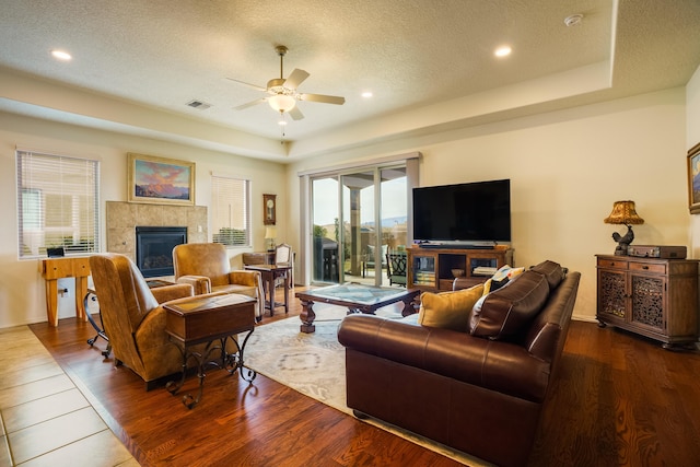 living area featuring visible vents, a tray ceiling, a textured ceiling, wood finished floors, and a tile fireplace