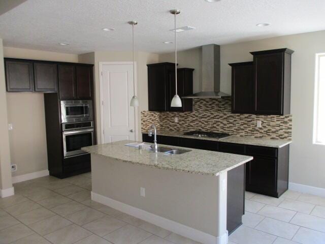 kitchen featuring wall chimney range hood, a sink, appliances with stainless steel finishes, and decorative backsplash