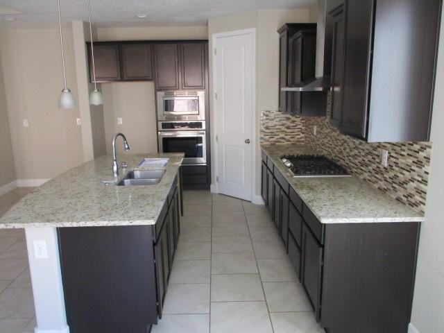 kitchen featuring light tile patterned floors, decorative backsplash, appliances with stainless steel finishes, a sink, and an island with sink