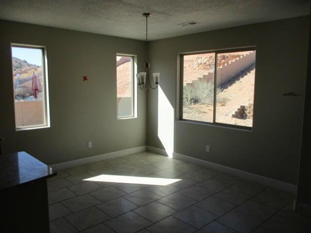 empty room with a textured ceiling, baseboards, a chandelier, and a wealth of natural light