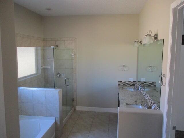 full bath with double vanity, a shower stall, tile patterned flooring, baseboards, and a bath