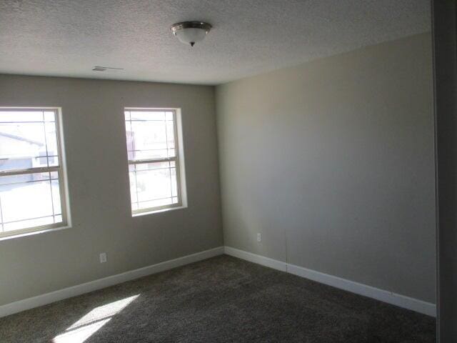 unfurnished room featuring a textured ceiling, dark carpet, and baseboards