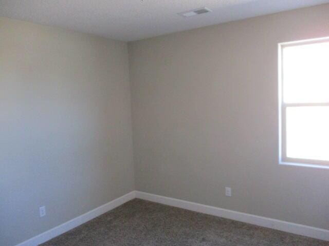 empty room featuring carpet, visible vents, and baseboards