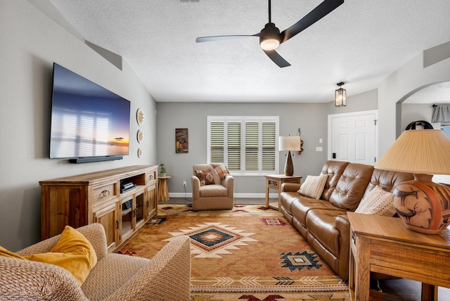 living area with a textured ceiling, ceiling fan, arched walkways, and baseboards