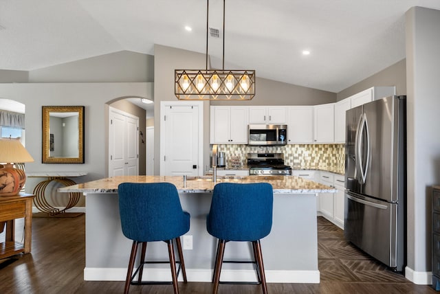 kitchen featuring white cabinets, a breakfast bar, light stone countertops, stainless steel appliances, and backsplash