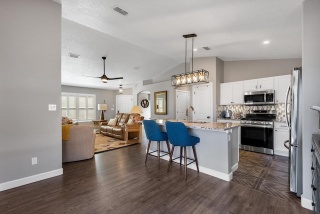 kitchen featuring visible vents, white cabinets, appliances with stainless steel finishes, light stone countertops, and a kitchen bar