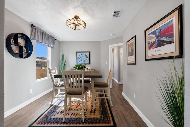 dining space with visible vents, a textured ceiling, baseboards, and wood finished floors