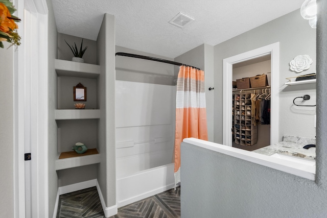 full bath featuring a textured ceiling, a walk in closet, visible vents, and shower / tub combo with curtain