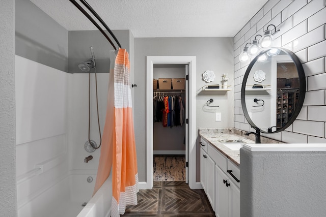 bathroom with baseboards, a spacious closet, shower / bath combo with shower curtain, a textured ceiling, and vanity