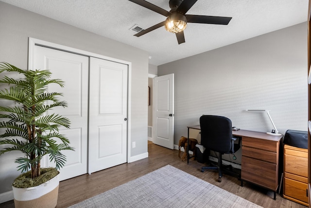 office featuring a textured ceiling, wood finished floors, a ceiling fan, visible vents, and baseboards