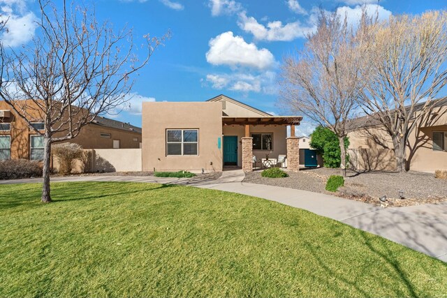 pueblo-style home with stucco siding, a front lawn, and fence