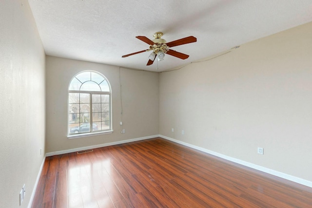 empty room with a textured ceiling, wood finished floors, visible vents, and baseboards